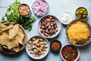 ingredients for texas style nachos, cheese, steak, chicken, chips, pickled jalapeños