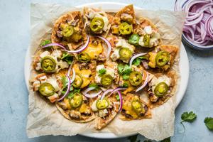 Texas style nachos on a platter topped with refried beans, cheese, steak, chicken and jalapeños