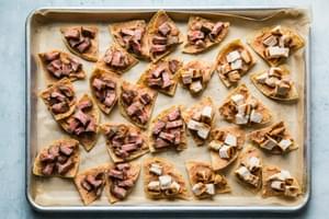 tortilla chips on a baking sheet topped with refried beans, cheese, steak, chicken