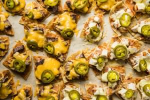 tortilla chips cooked on a baking sheet topped with refried beans, cheese, steak, chicken and jalapeños
