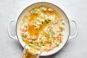 spices, milk and chicken stock being added to a skillet with onion, celery, carrots and butter