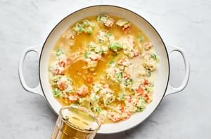 spices, milk and chicken stock being added to a skillet with onion, celery, carrots and butter
