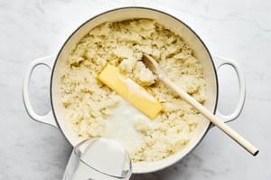 boiled potatoes being mashed with butter, milk, garlic powder, salt and pepper