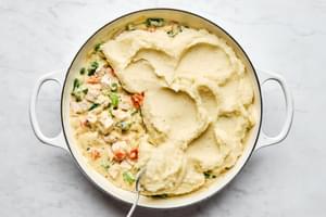 garlic mashed potatoes being spread on top or turkey shepherds pie filling with carrots, onion, celery and greenbeans