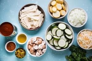 Olive oil, vegetables, Taco seasoning, green chilies, enchilada sauce, Corn tortillas, and Cheese in bowls on the counter