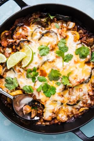 Homemade vegetarian enchilada skillet topped with melted cheese, cilantro and lime wedges in a skillet on the counter