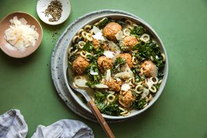 5-ingredient chicken meatball soup with kale and parmesan in a bowl with a spoon next to small bowls of parmesan and pepper