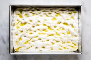 homemade focaccia bread dough ready to bake in a baking dish with olive oil