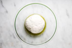 homemade focaccia bread dough rising in a bowl with olive oil