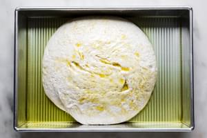 homemade focaccia bread dough in a baking dish with olive oil