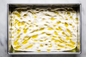 homemade focaccia bread dough dimpled in a baking dish with olive oil