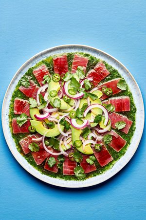 homemade aguachile on a serving platter. layered cilantro sauce, tuna, avocado slices, red onion and Serrano peppers