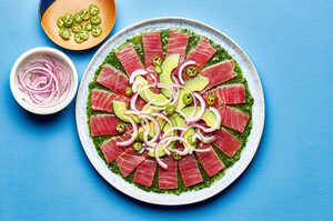 homemade aguachile on a serving platter. layered cilantro sauce, tuna, avocado slices, red onion and Serrano peppers