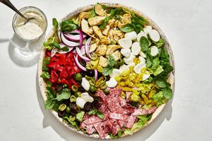 antipasto salad with romaine, salami, mozzarella, basil, and pickled veggies next to a bowl of creamy parmesan lemon dressing