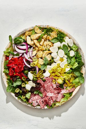 antipasto salad with romaine, salami, mozzarella, basil, red onion, olives, artichoke hearts and pepperoncinis