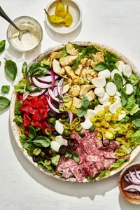 antipasto salad with romaine, salami, mozzarella, basil, and pickled veggies next to a bowl of creamy parmesan lemon dressing