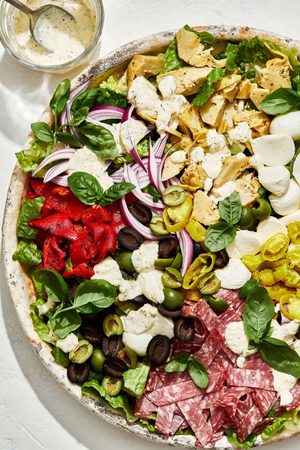 antipasto salad with romaine, salami, mozzarella, basil, and pickled veggies next to a bowl of creamy parmesan lemon dressing