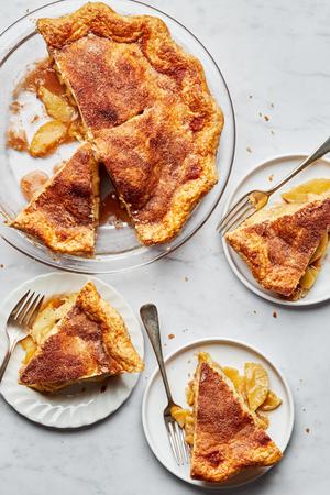 a homemade apple pie with golden crust in a pie pan with slices that have been cut out and served on plates with forks