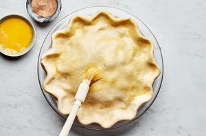 beaten egg being brushed onto a raw apple pie using a pasty brush