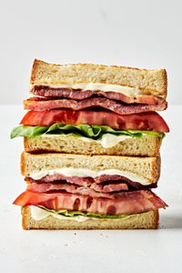 two halves of a BLT with homemade mayonnaise stacked on top of each other on the counter