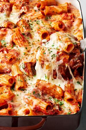 homemade baked rigatoni being scooped out of a 9x13 casserole dish