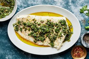 homemade Baked Cod with Parsley Olive Tapenade on a serving plate with a serving fork next to a bowl of extra tapenade