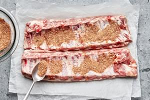 homemade dry rub being spooned over raw pork ribs on top of parchment paper