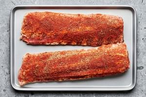raw pork ribs covered in homemade dry rub on a baking sheet ready to be baked in the oven
