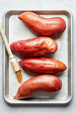 4 sweet potatoes on a sheet pan being brushed with olive oil