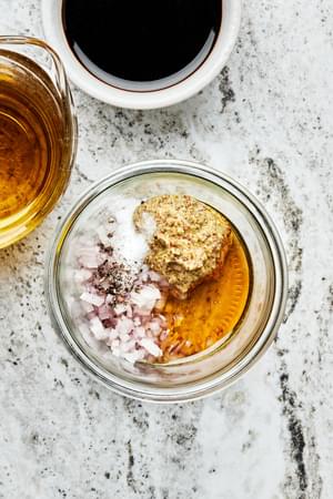 mustard, honey, shallot, salt, and pepper in a mason jar next to bowls of balsamic vinegar and olive oil to make vinaigrette
