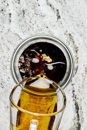 olive oil being poured into a mason jar with mustard, honey, balsamic vinegar, shallot, salt, and pepper