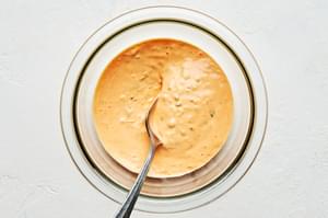 sriracha mayo in a glass bowl with a spoon made with Mayonnaise,
Garlic, Fish sauce, Scallions, Sriracha and Sugar