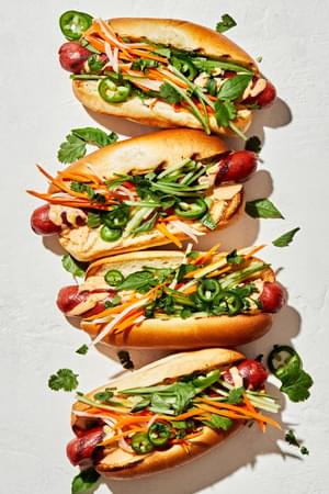 Banh Mi Hot Dogs drizzled with sriracha mayo topped with pickled veggies, cilantro, basil, cucumbers and jalapeños