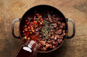 carrots, onion, celery, tomato paste, bouillon, thyme, beef stock, soy sauce and beef being cooked in a pot