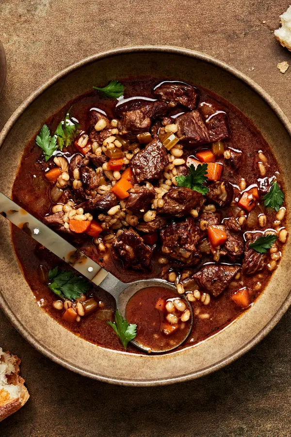 a bowl of homemade Beef & barley soup with spoon made with vegetables, spices, broth, tomato paste and soy sauce