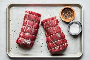 beef tenderloin wrapped in twine being seasoned with salt and pepper on a baking sheet