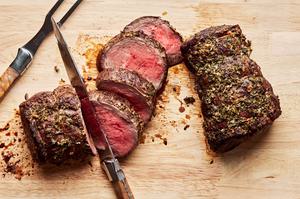 homemade beef tenderloin cooked with garlic herb butter being sliced on a wood cutting board