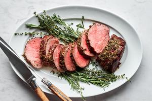 homemade beef tenderloin cooked with garlic herb butter sliced on a serving platter garnished with fresh herbs