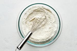 flour, sugar, cornstarch, baking powder, and salt being whisked together in a glass bowl for Belgian waffle mix