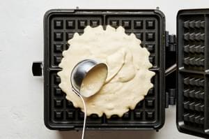waffle batter being ladled into a hot waffle iron