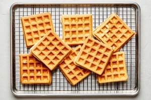 homemade golden brown belgian waffles being piled on a baking sheet to keep warm