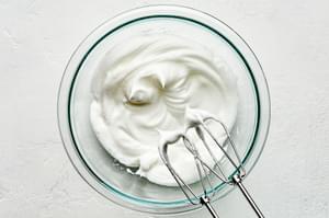 egg whites being whisked in a glass bowl with electric beaters until white peaks are formed
