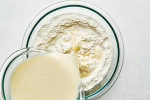 egg yolk and milk mixture being poured into a bowl of flour, sugar, cornstarch, baking powder, and salt