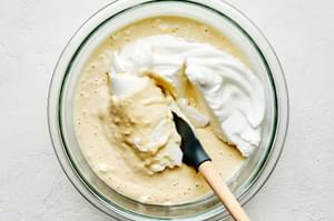 whipped egg whites being stirred into waffle batter to make homemade Belgian waffles