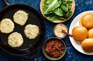 homemade black bean burger patties topped with melted pepper jack cheese in a skillet next to bowls of burger fixings