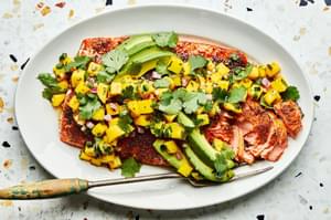 blackened salmon topped with homemade mango salsa and avocado on a serving plate with a serving fork