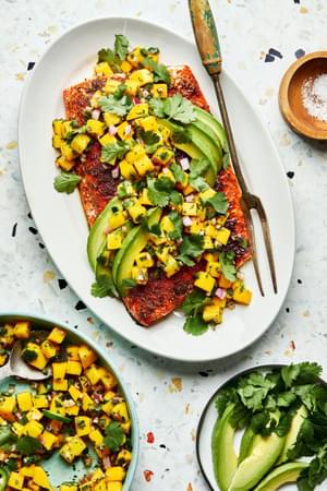 blackened salmon with homemade mango salsa and avocado on a serving plate next to bowls of mango salsa and avocado