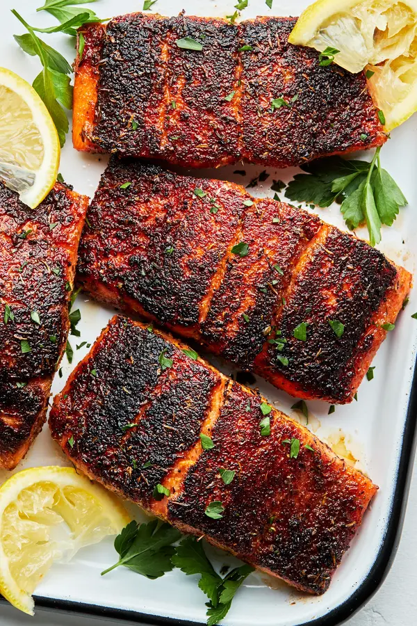 three 4 ounce Blackened salmon fillets on a serving platter with lemon wedges and sprinkled with fresh parsley