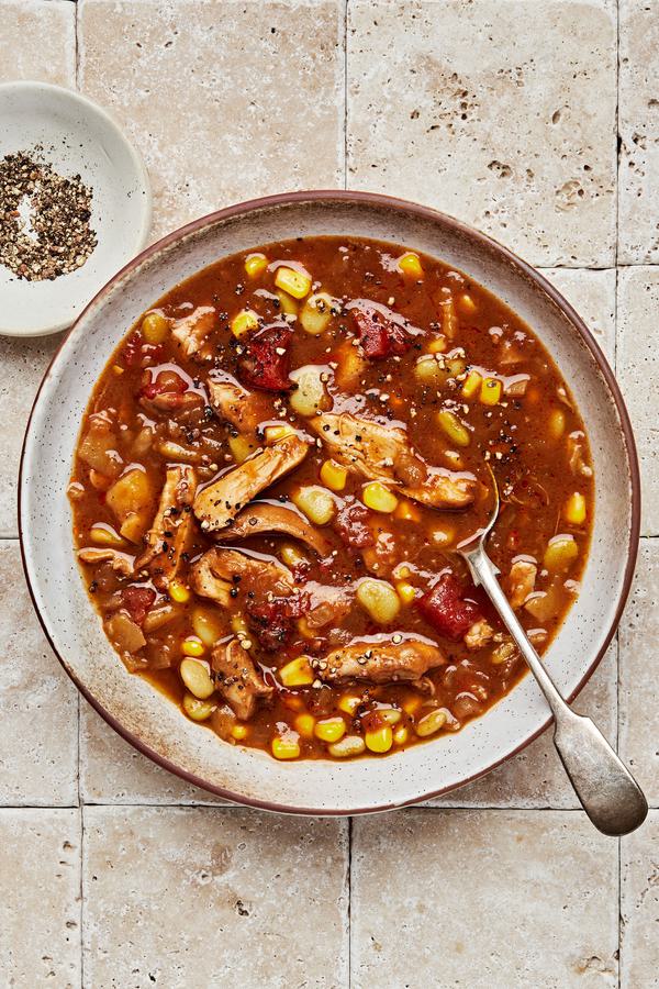 a bowl of homemade Brunswick stew with a spoon next to a small bowl of cracked pepper for serving