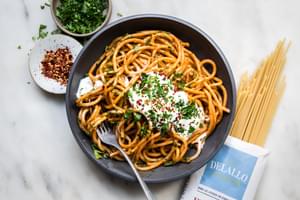 spicy roasted red pepper sauce with whipped feta on top of bucatini pasta next to a bag of delallo dry bucatini & parsley